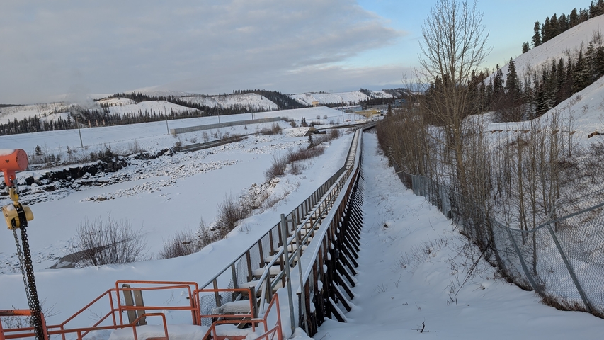 Long industrial conveyor stretching across a snowy valley toward distant hills.