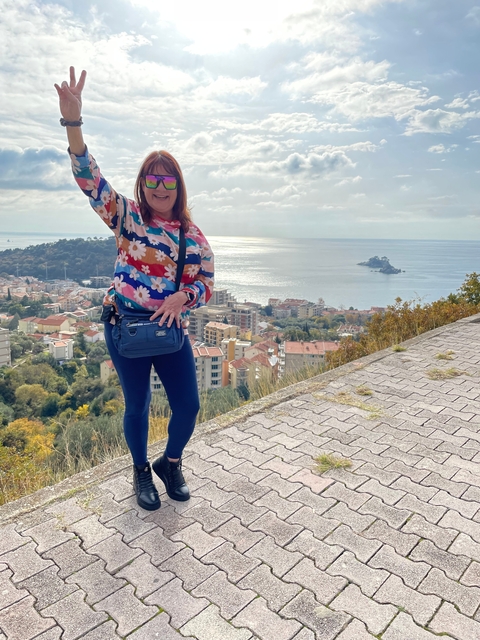 A woman with a colorful sweater posing with a scenic view of buildings and water.