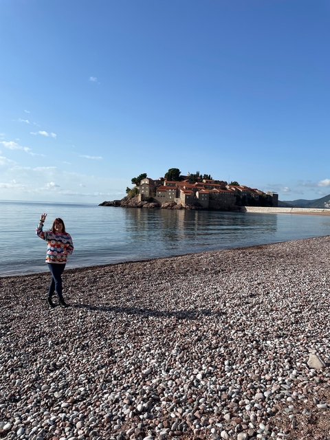 A person on a pebble beach with a background of a small island castle.