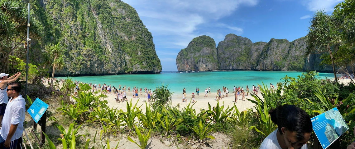 Crowded beach with clear water and limestone cliffs.