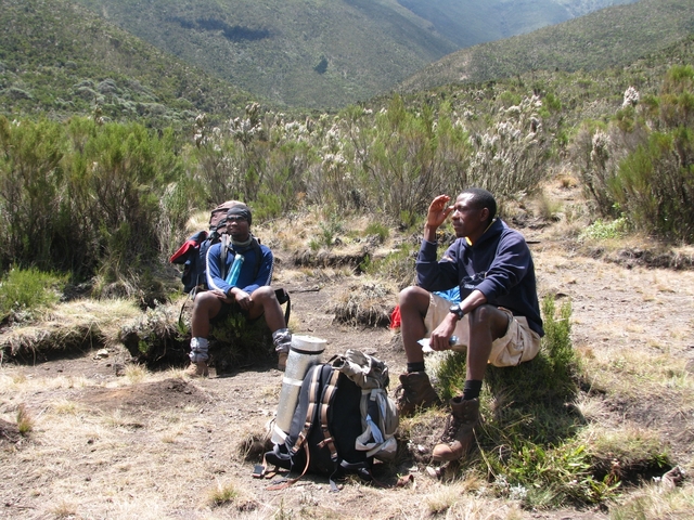 Two hikers resting on grass in a mountainous environment.