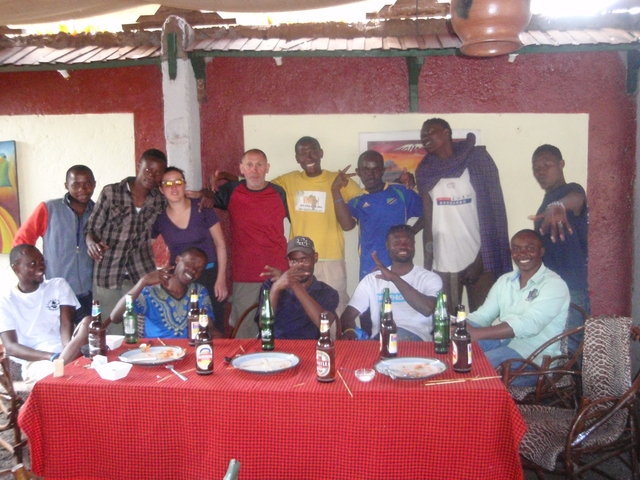 Large group of people posing indoors, drinks on the table.