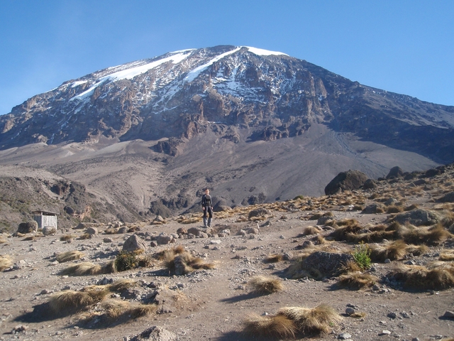 Mount Kilimanjaro prominently visible with an adventurer in the foreground.