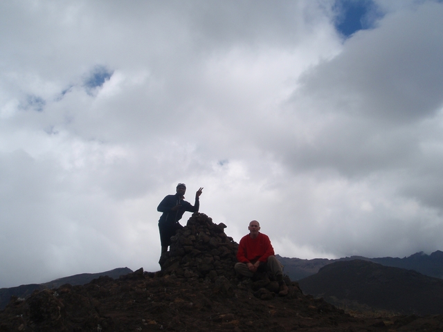 Two people on rocky terrain under a cloudy sky.