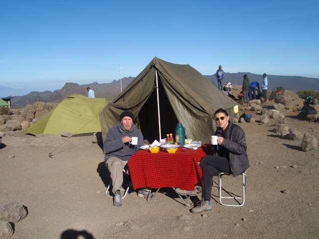 Two people sitting at a table with a tent in the background.