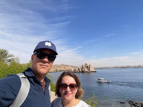Couple posing by a river with a boat and rocky landscape.