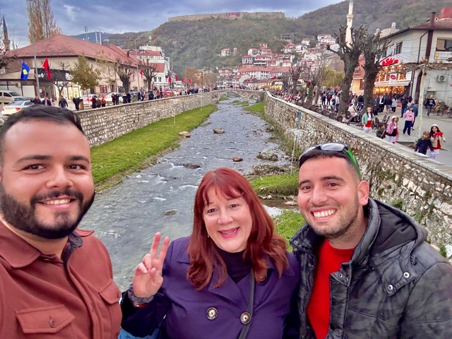 Three people smiling and posing by a river in a busy street.