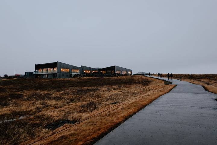 Pathway leading to a building with warm lights in a barren landscape at dusk.