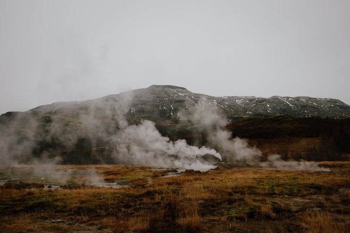 Geothermal field with steam rising against a mountainous backdrop.