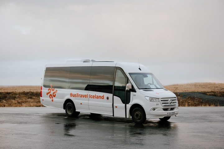 White tour bus parked in an open area with a cloudy sky.
