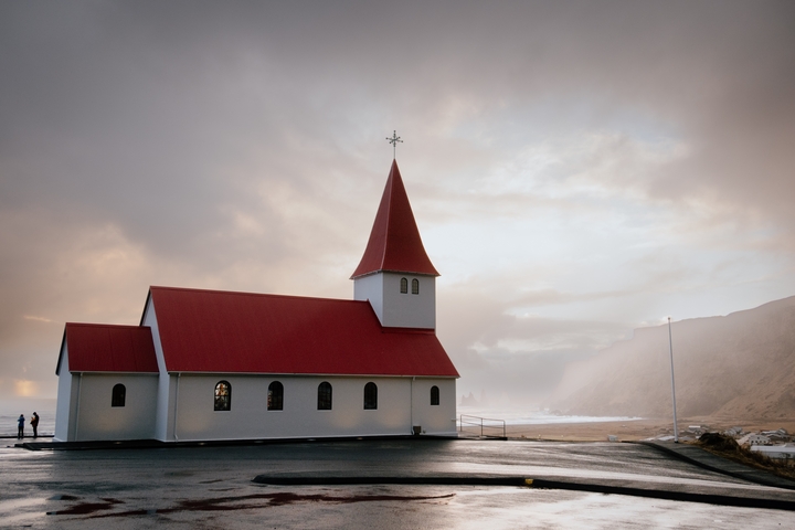 White church with a red roof near a beach during sunset.