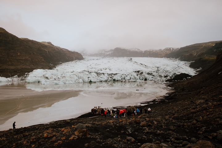 Glacier with a group of people in the foreground, cloudy sky.