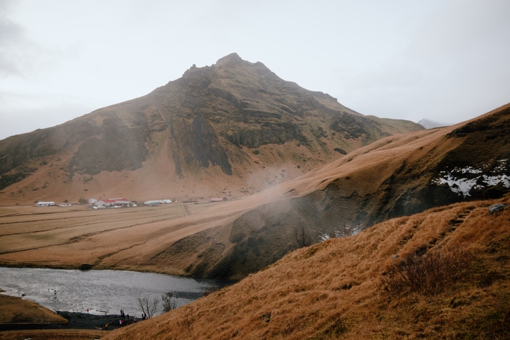 Mountain landscape with a river and scattered rural buildings.