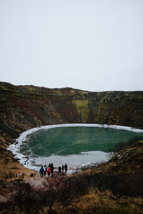 Crater with colorful rocky walls and a frozen lake.