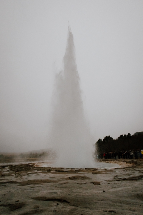 Geothermal geyser erupts in a splash against a cloudy sky.
