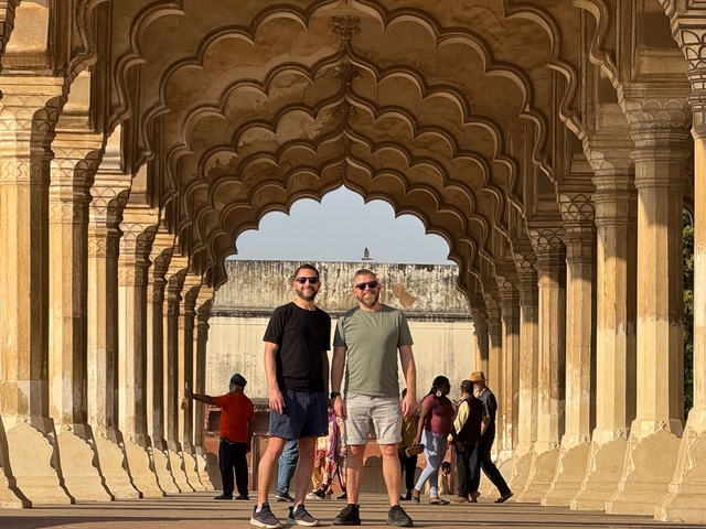 Two men standing in a historical site with arched architecture.