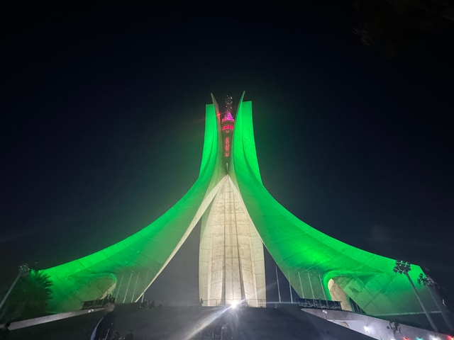 Monument illuminated with green lights against a night sky.
