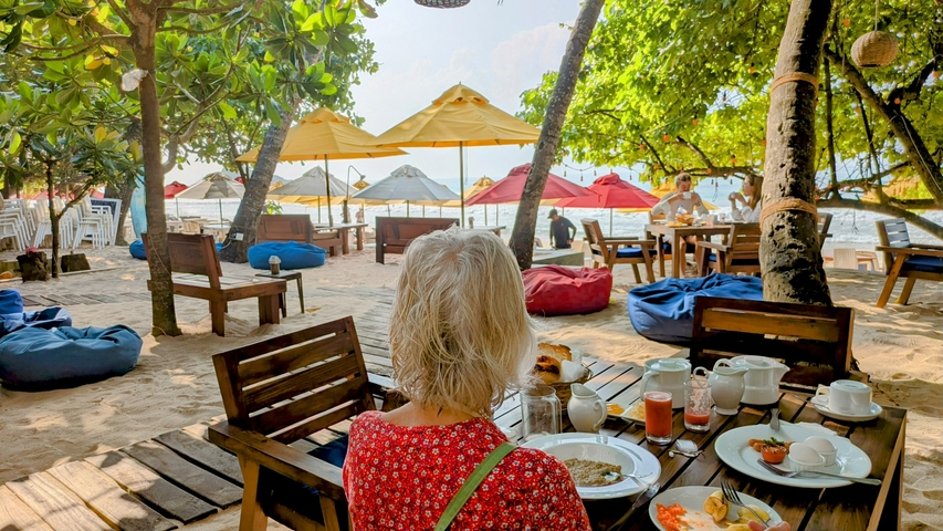 Person dining outdoors at a beachside restaurant with colorful umbrellas.