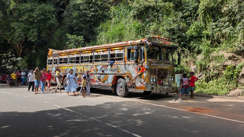 Colorful, decorated bus with people standing around it on a rural road.