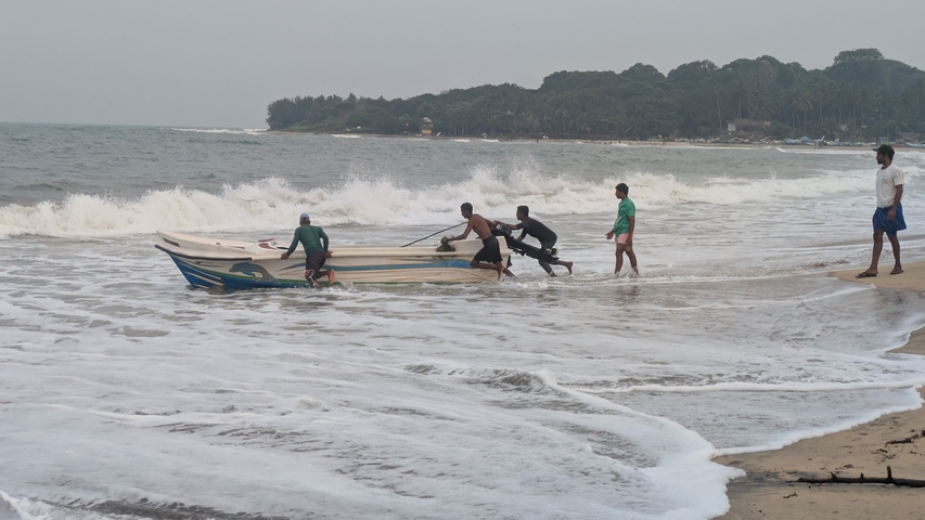 Group of people pushing a boat into the ocean on a sandy beach.