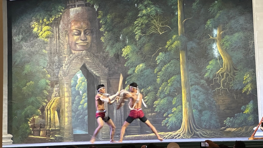 Two performers engaged in a traditional martial arts performance in front of a mural.