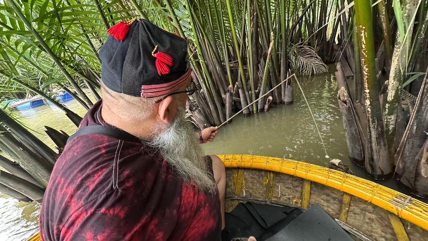 A person fishing from a small boat amidst lush greenery.