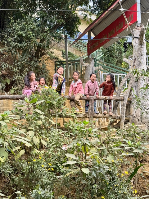 Group of children sitting on a wooden railing in a natural setting.