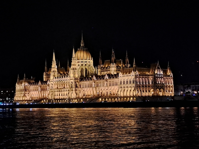 Night view of a brightly lit historic building with a reflection on water.