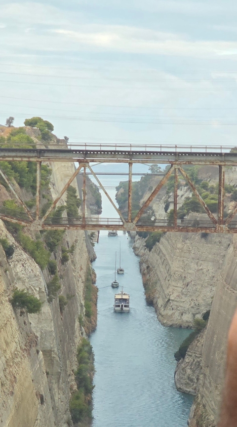 View of a deep canal under a rusty bridge with small boats passing through.