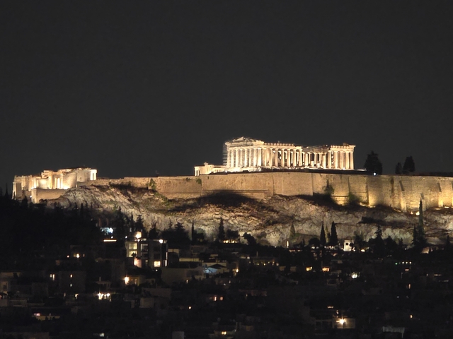 Night view of a lit Acropolis against a dark sky.