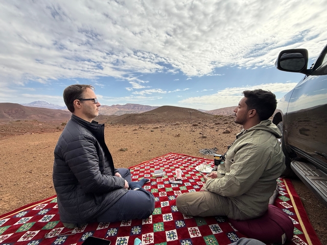 Two people sitting on a red patterned rug in a desert landscape.