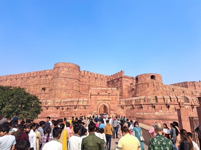 A crowd in front of a large red sandstone fort.