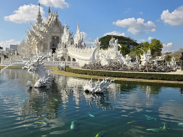 A white temple with detailed sculptures and a reflective pond in front.