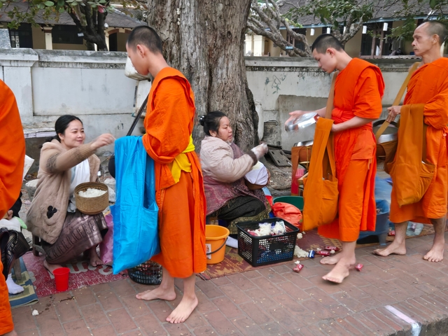 People in traditional robes receiving alms on a street.