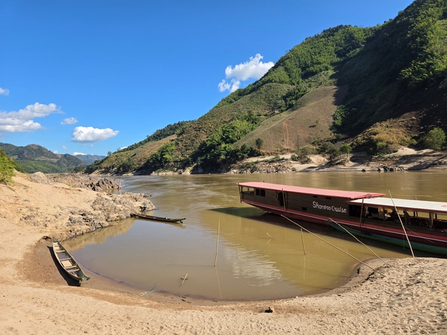 Boats docked along a river with scenic hills in the background.