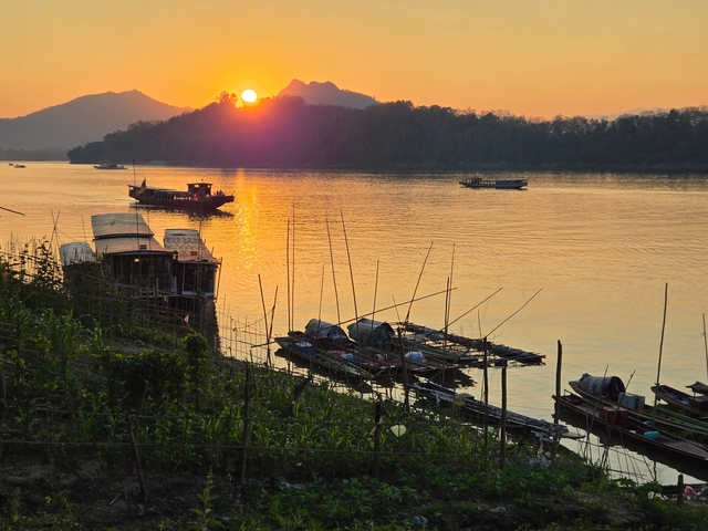 Sunset over a river with boats and orange skies.