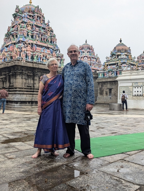 Older couple in traditional attire in front of a temple.