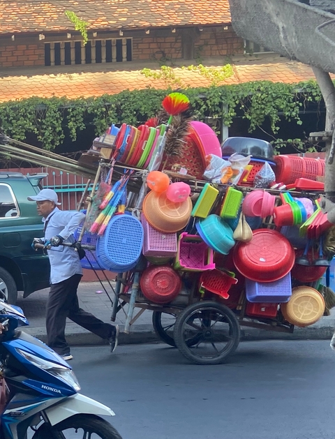 Man pushing a bicycle loaded with colorful plastic goods.