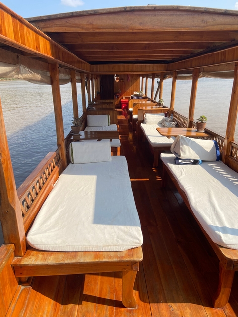Wooden boat interior with cushioned seats near water.