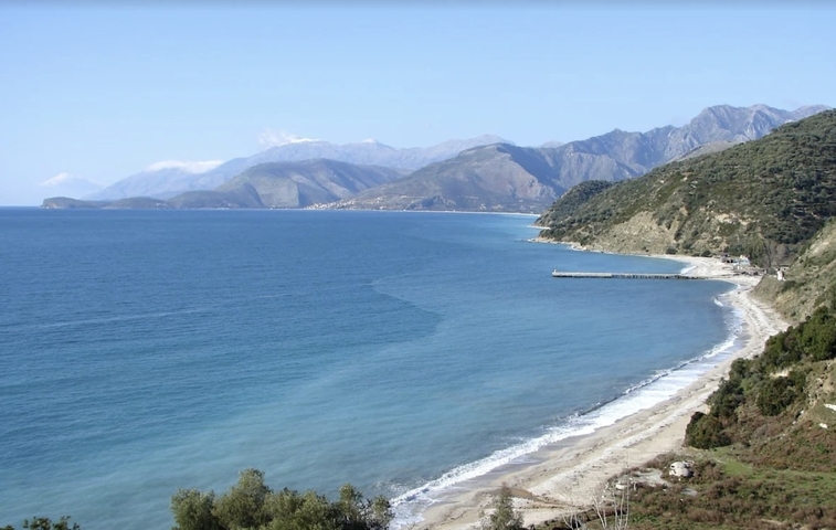 Coastal area with a curve of sandy beach and hills.