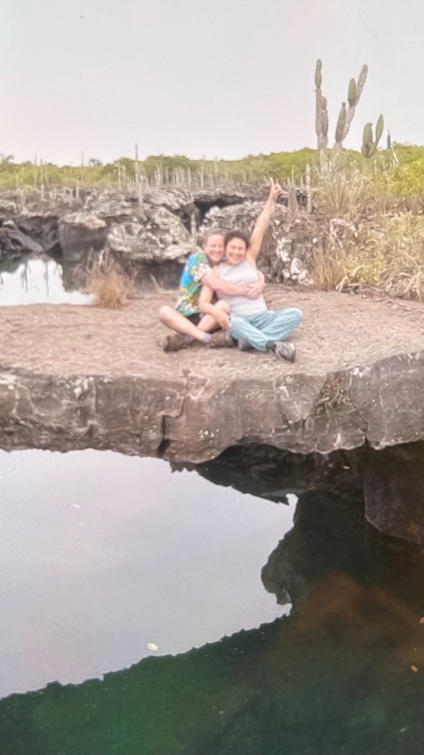 Blurry image of two people sitting on rocky terrain beside water.