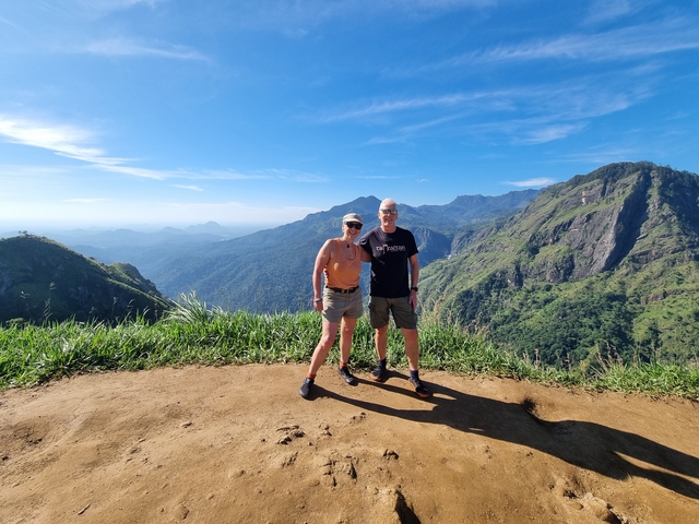 Two people standing on a hilltop with mountains in the background.