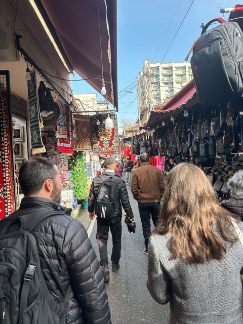 Market alley with people and colorful textiles hanging.