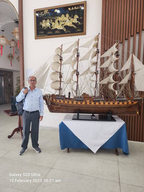 A man posing next to a model ship.