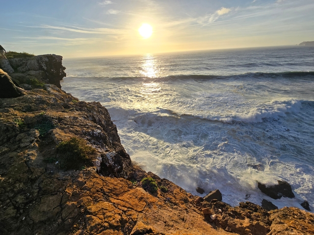 Rocky coastline at sunset with waves crashing.
