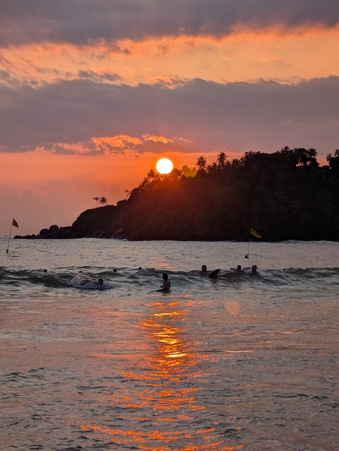 People swimming in the ocean at sunset near a tropical island.