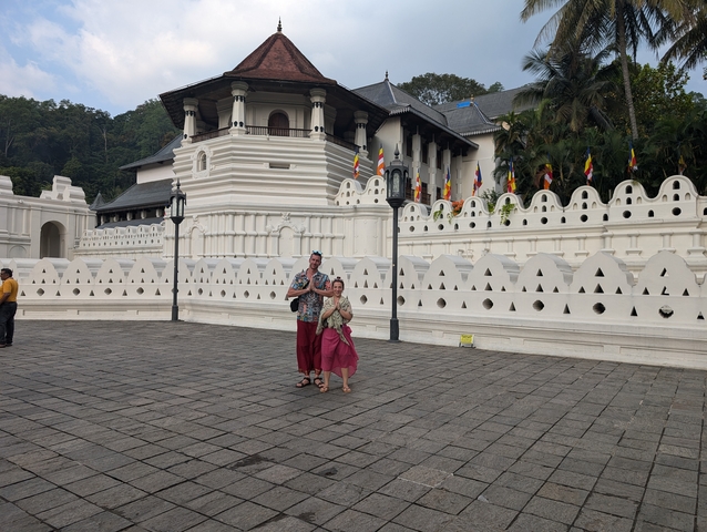Couple standing in front of a white temple with flags.