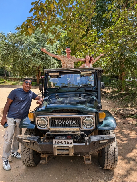 Three people posing with a classic jeep in a natural setting.