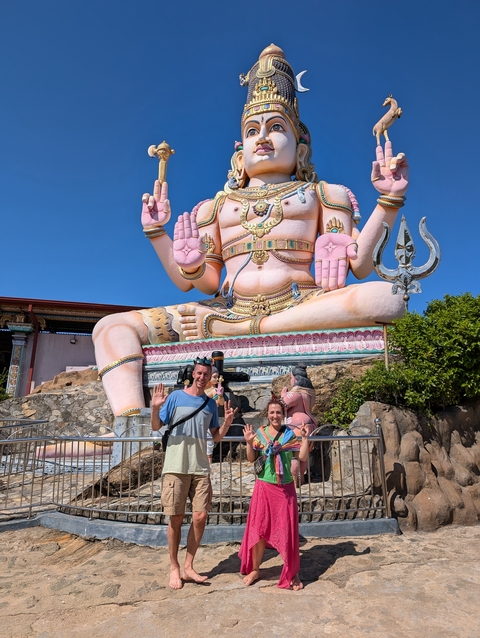 Two people posing in front of a large Hindu deity statue.