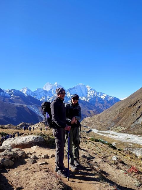 Two travelers posing with trekking poles against a backdrop of snow-covered peaks.